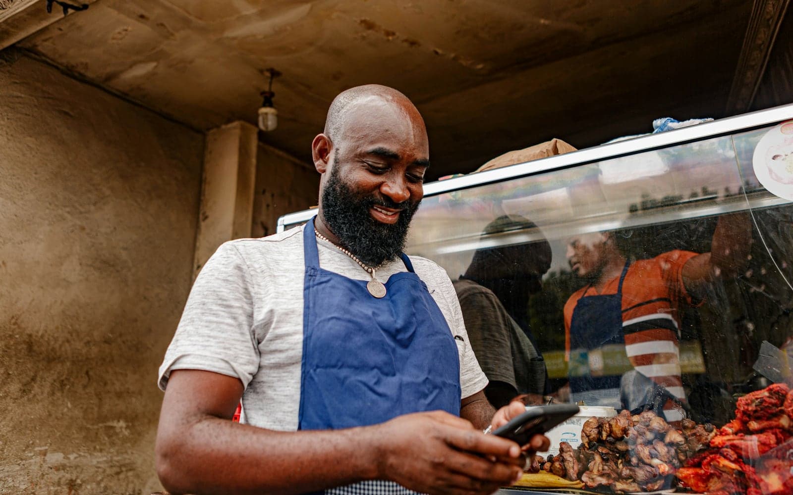 A food stall owner in an apron checking his phone