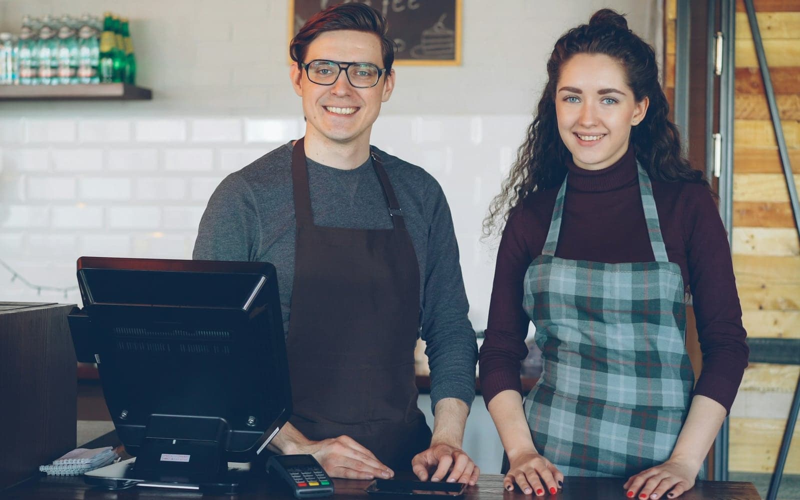 Two café staff smiling behind the counter, beside the till