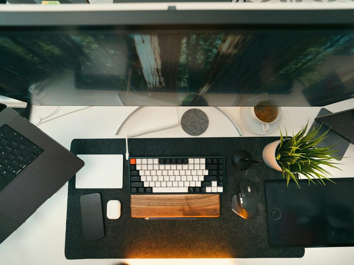A designer's desk from above, with a keyboard, a laptop and a large monitor