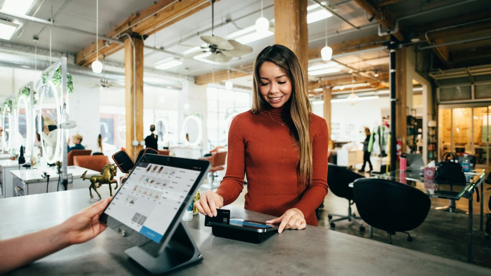 A customer paying at the counter of a bright café, smiling at the person serving her